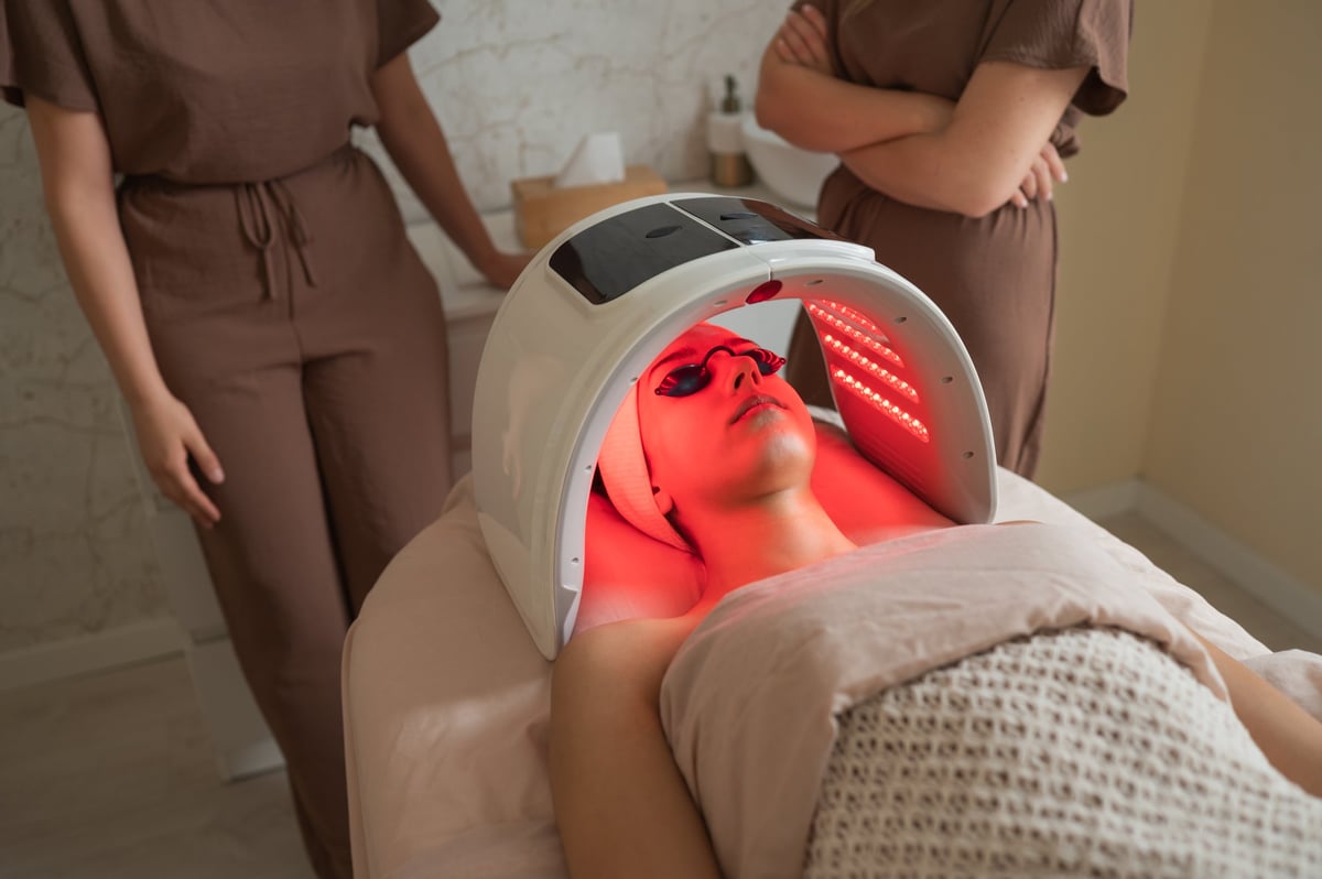 Young woman lying down receiving led light therapy by a professional beautician in a wellness center